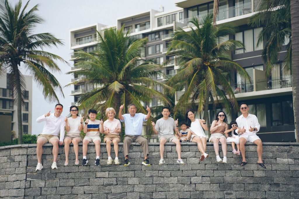 Lächelnde Familie beim Mehrgenerationen-Urlaub am Strand; Großeltern und Enkelkinder beim Wandern in den Bergen; Familienmitglieder verschiedener Generationen beim gemeinsamen Kochen in einem Ferienhaus; Drei Generationen sitzen lachend an einem Tisch und planen die Reise.