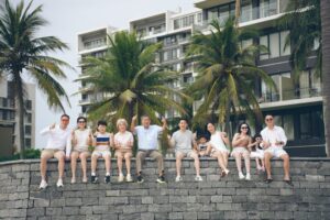 Lächelnde Familie beim Mehrgenerationen-Urlaub am Strand; Großeltern und Enkelkinder beim Wandern in den Bergen; Familienmitglieder verschiedener Generationen beim gemeinsamen Kochen in einem Ferienhaus; Drei Generationen sitzen lachend an einem Tisch und planen die Reise.